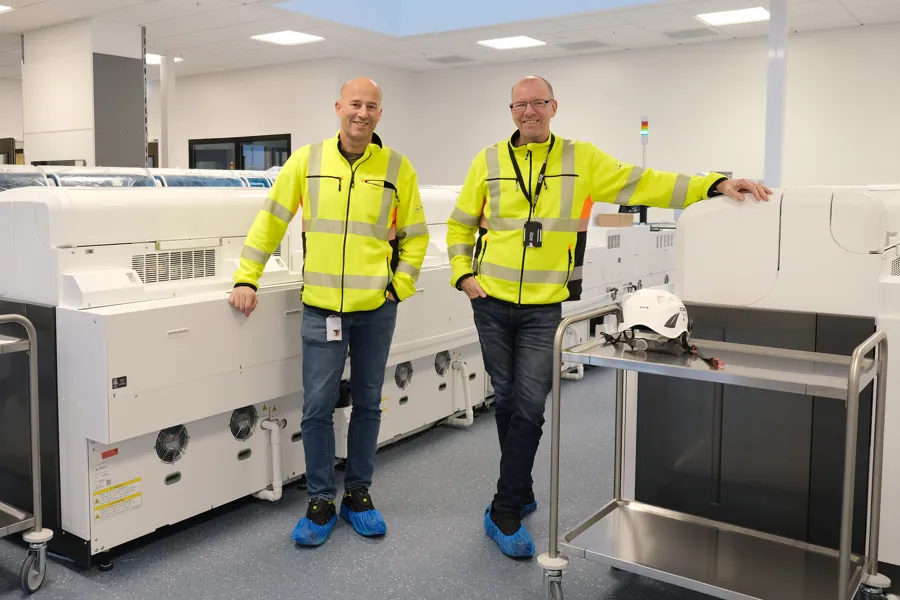 Menn i gule jakker som står ved siden av en maskin
